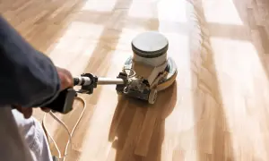 En person slipar parkettgolv med en maskin. Dammet virvlar upp när golvet blir rent och redo för behandling.
