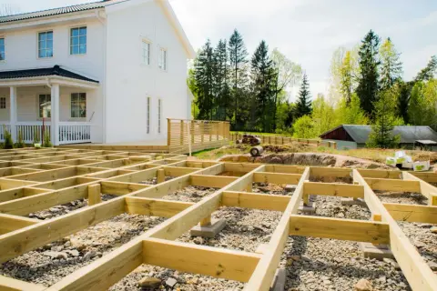 Grundarbete för att bygga altan på mark. Träkonstruktionen är på plats framför ett vitt hus.