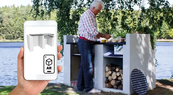 Man förbereder mat vid en murad grillplats vid en sjö. En mobil visar en 3D-modell av grillplatsen i AR.