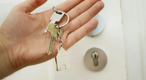 En hand håller nycklar med ett hus som berlock. Dags att byta lås och få nya nycklar till hemmet.