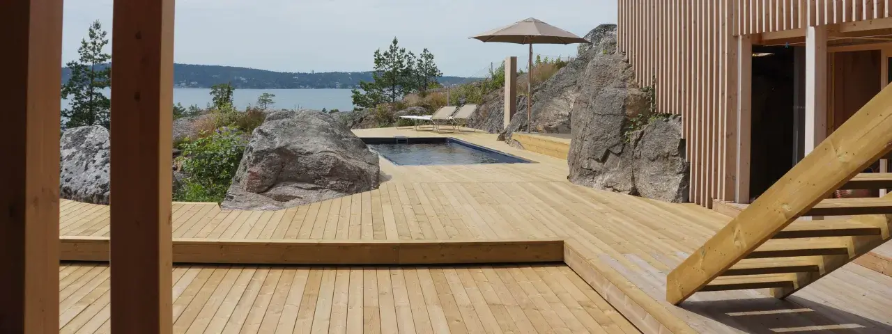 En stor altan i trä med pool och solstolar, omgiven av klippor och med utsikt över havet. Trall mått är perfekt för detta sommarparadis.