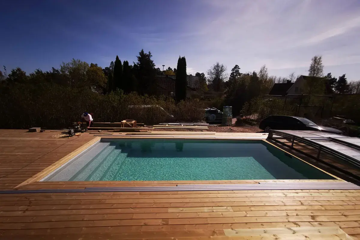 Arbetare bygger in pool med trädäck. Vattnet glittrar i solen. Snart redo för bad!