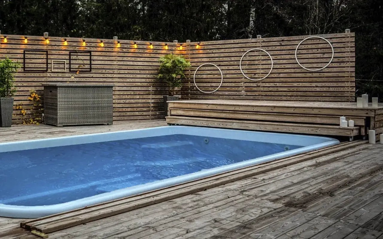 En avkopplande oas med en pool omgiven av trall. Träpanelen bakom poolen är dekorerad med ljusslinga och cirklar.