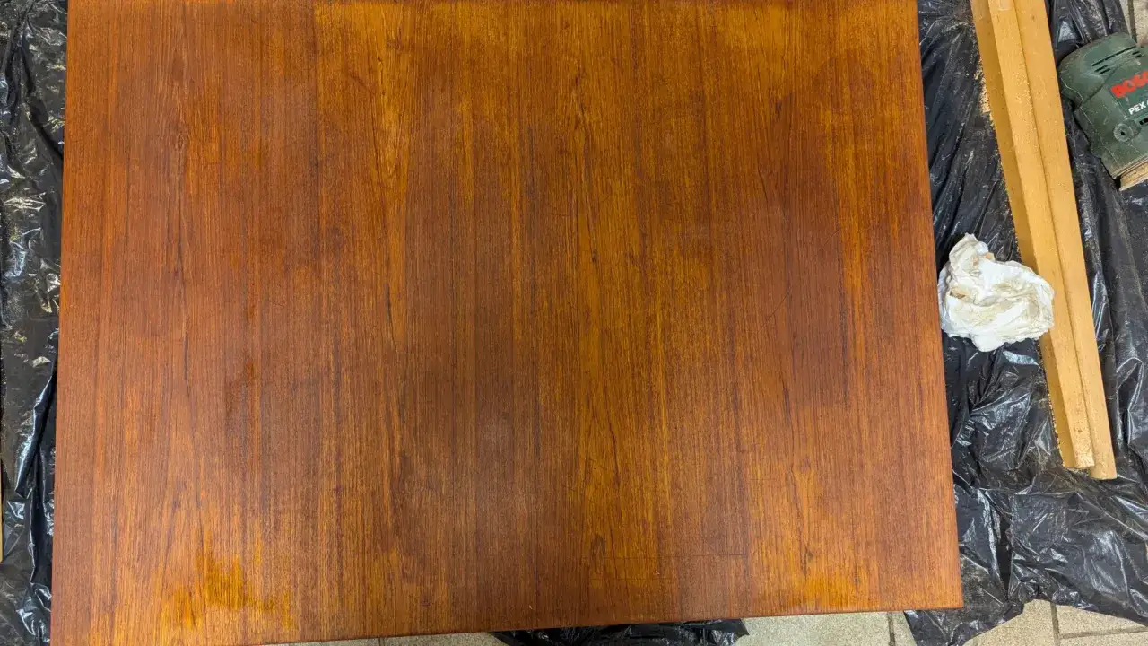 Förbereder för att slipa teakbordet. En slipmaskin och trasor ligger redo på plast.