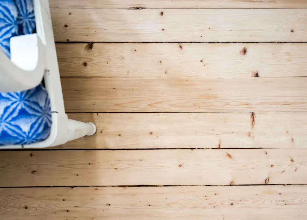 Ett vitt möbelben vilar på ett ljust, såpskurat golv av trä. Blåmönstrad textil syns i bakgrunden.