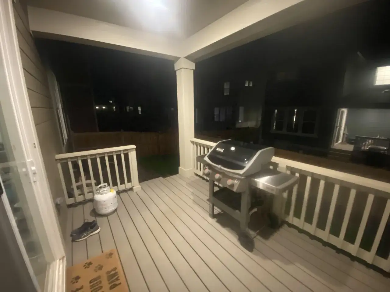 En gasolgrill under tak på en altan, redo för grillkvällar. Bredvid står en gasoltub och ett par skor.
