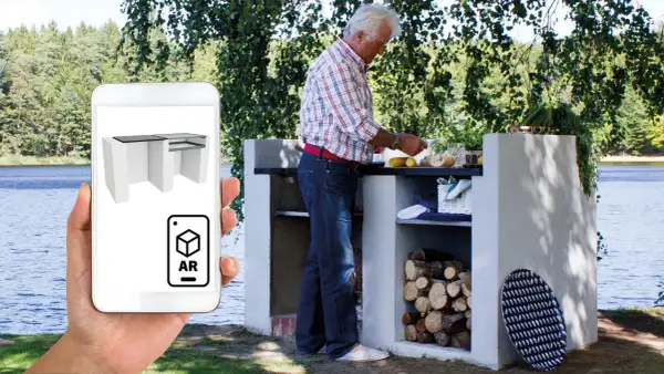 Man förbereder mat vid en murad grillplats vid en sjö. En mobil visar en 3D-modell av grillplatsen i AR.